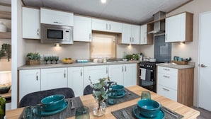 A modern kitchen with white cabinets, a microwave, stove, and a dining area with a table set for four. - Waterside Haven (Northampton)
