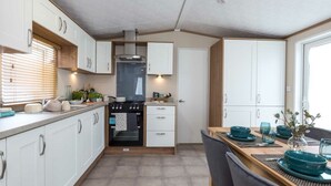 A compact kitchen with white cabinets, a stove, and a dining area with teal bowls and a vase. - Waterside Haven (Northampton)