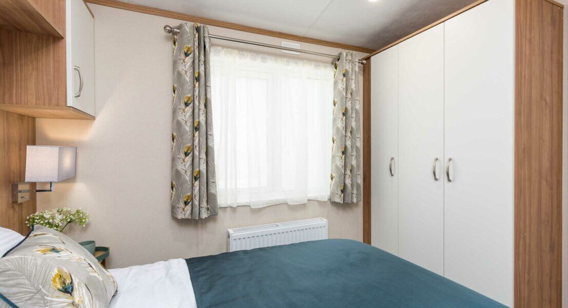 A bedroom with a bed, a window with curtains, a radiator, and a wardrobe.