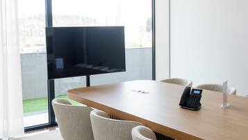 A conference room with a large table, four chairs, a phone, and a TV on the wall.