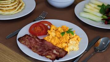 Une assiette de petit-déjeuner comprenant des œufs brouillés, du bacon, des tomates et une salade en accompagnement.