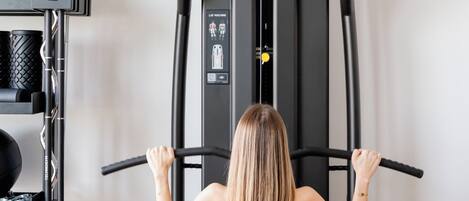 Une femme utilise un appareil de musculation doté d’une barre de traction, entourée d’autres équipements de fitness.