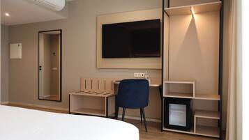 A modern hotel room with a bed, a desk, a chair, a TV, and built-in shelving.