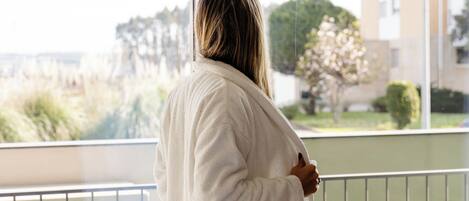 Una persona in veste bianca su un balcone con vista su un edificio e vegetazione.