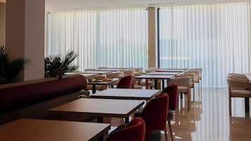 A modern dining area with tables and chairs, large windows with blinds, and a ceiling with a dotted pattern.