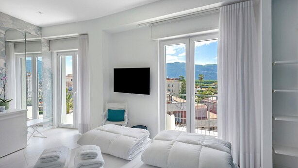 A modern hotel room with a bed, a TV, a balcony with a city view, and a bathroom with a mirror and sink. - Room 'Superior Terra' with Mountain View, Wi-Fi and Air Conditioning (Pompei)