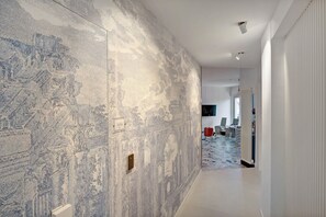 Un pasillo con pared texturizada, una puerta y una vista parcial de una habitación con radiador y televisor.