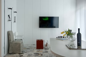 A modern living room with a TV, a striped chair, a red cabinet, a glass vase with flowers, and a wine bottle.