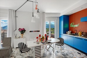 A modern kitchen with a blue accent wall, a dining area with striped chairs, and a view of mountains through the window.