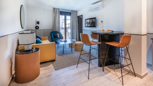 A compact hotel room with a sofa, a small dining table, and a bar area. - Superior 1 Bedroom Apartment (Sevilla)