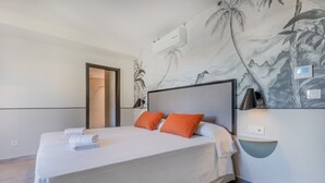 A neatly made bed with white linens and two orange pillows, a wall-mounted light, and a partial view of a bathroom. - Superior 1 Bedroom Apartment (Sevilla)