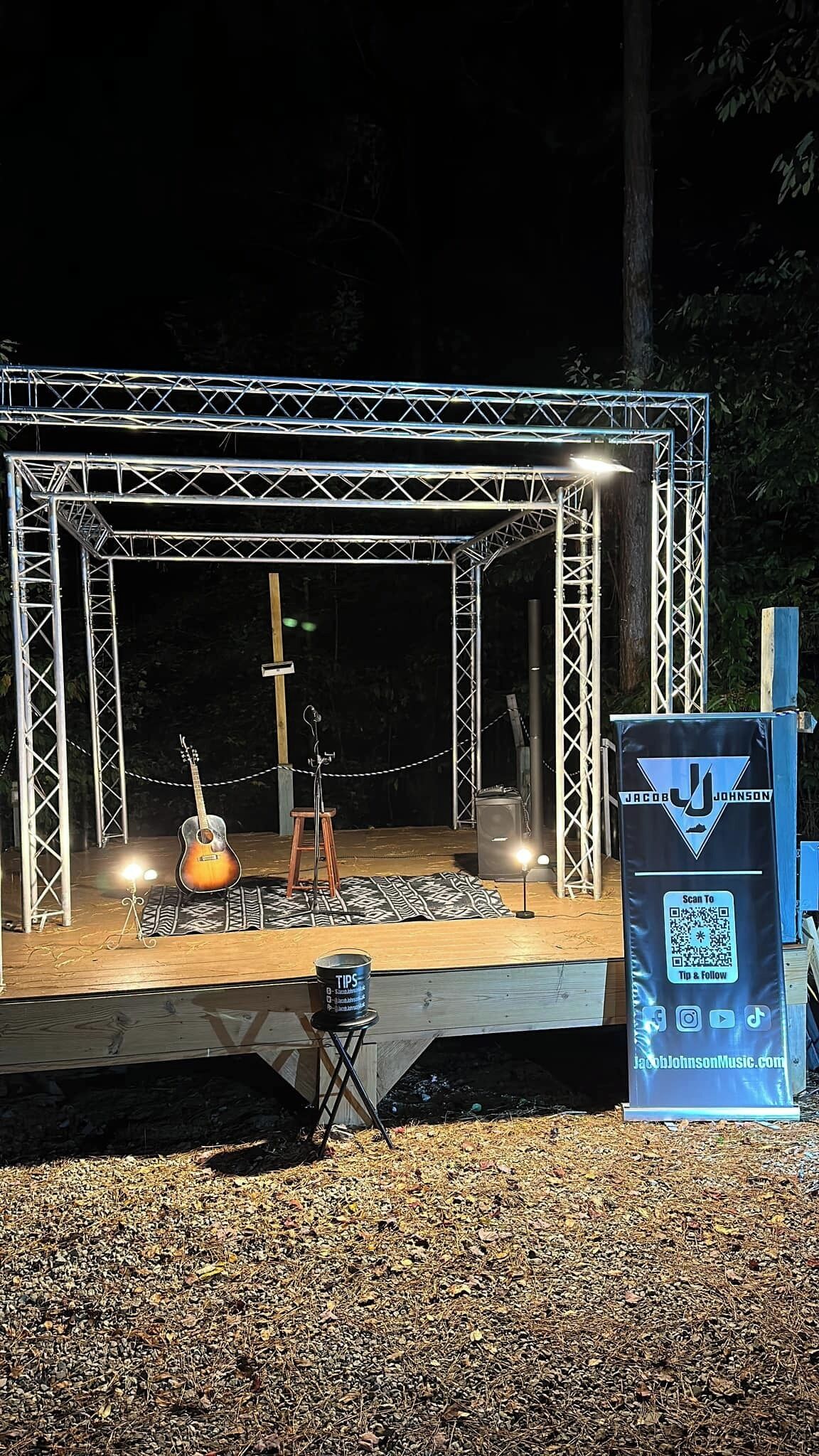 A stage with a guitar and stools, a QR code sign, and a metal structure.