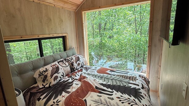 A cozy bedroom with a large bed, a window with a view of greenery, and wooden ceiling beams.