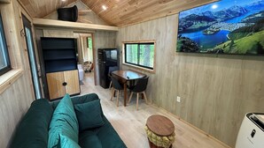 A compact living space with a wooden ceiling, a sofa, a dining table, and a refrigerator.