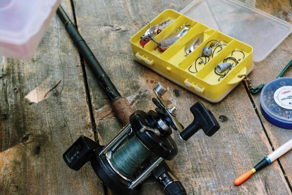 A fishing rod, reel, tackle box, and fishing line on a wooden surface. - Sasquatch Farm (South Pittsburg)