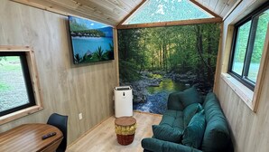 A cozy room with a wooden ceiling, a green sofa, a small table, and a TV on the wall.