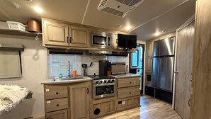 A compact kitchen with wooden cabinets, a microwave, a stove, and a refrigerator.