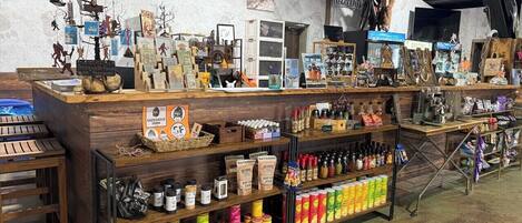 Interior rústico com prateleiras de madeira exibindo diversos produtos, uma placa com a inscrição
