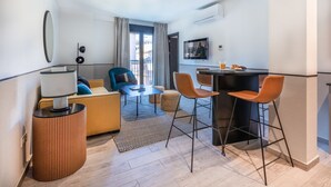 A compact hotel room with a sofa, a small dining table, and a bar area.
