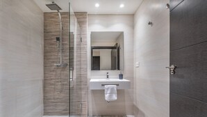 A modern bathroom with a glass-enclosed shower, a white sink, and a dark wooden door.