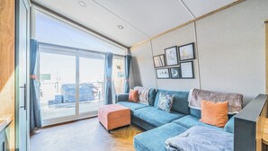 Uma sala de estar moderna com uma grande porta de vidro deslizante que dá para uma varanda, um sofá azul e piso de madeira.
