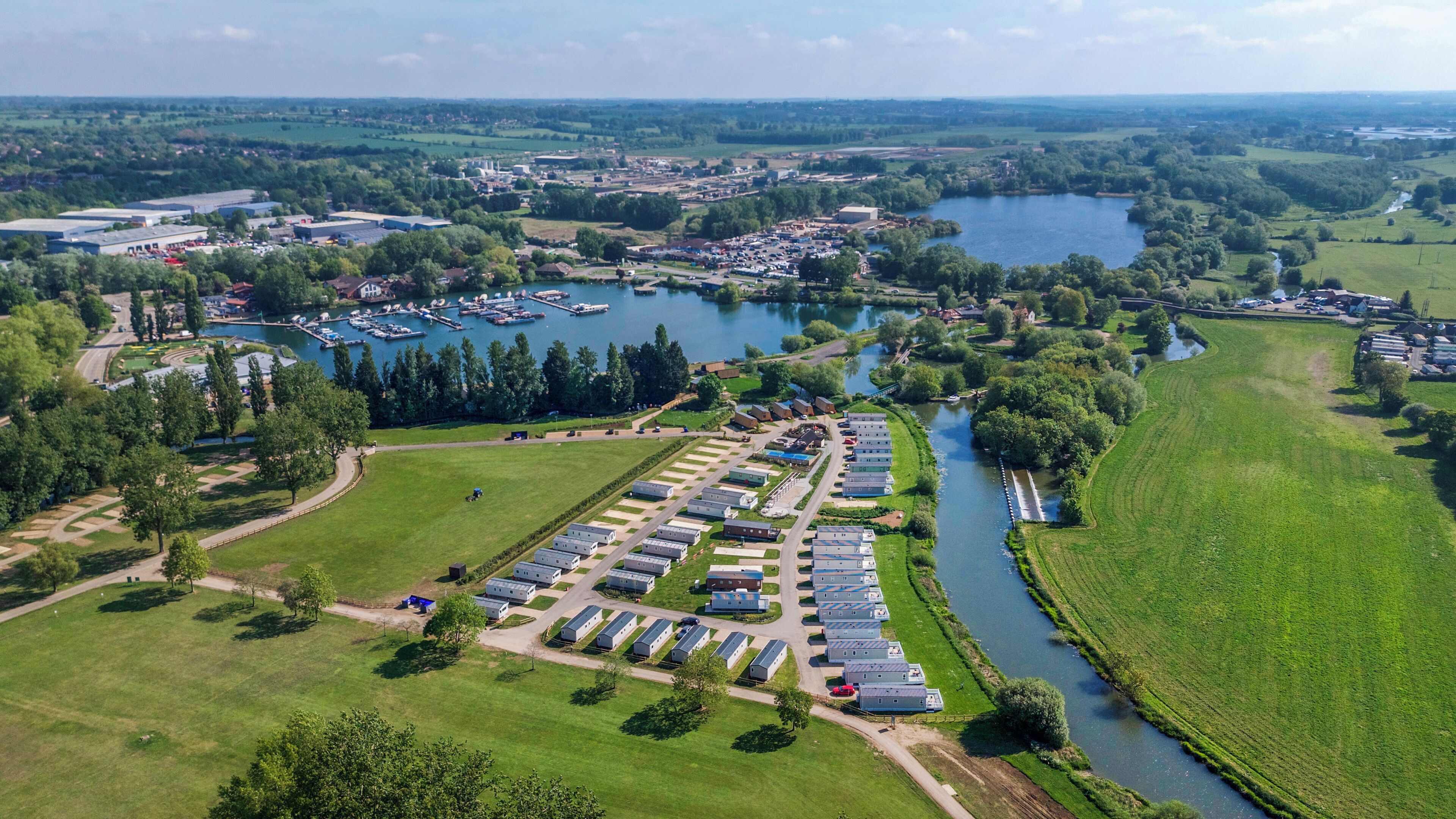 Vista aérea de um camping com veículos recreativos, um rio e vegetação ao redor.