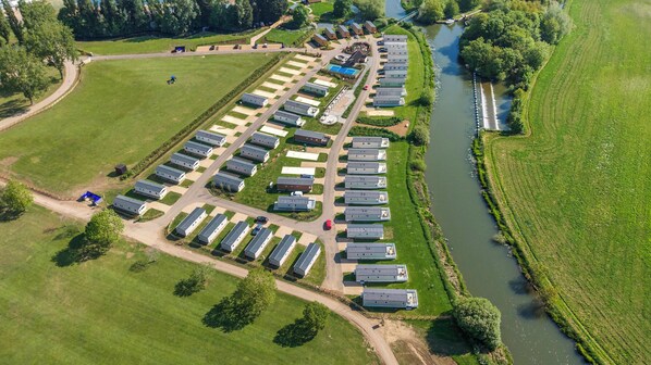 Vista aérea de un parque de caravanas con hileras de caravanas, un río y campos verdes.