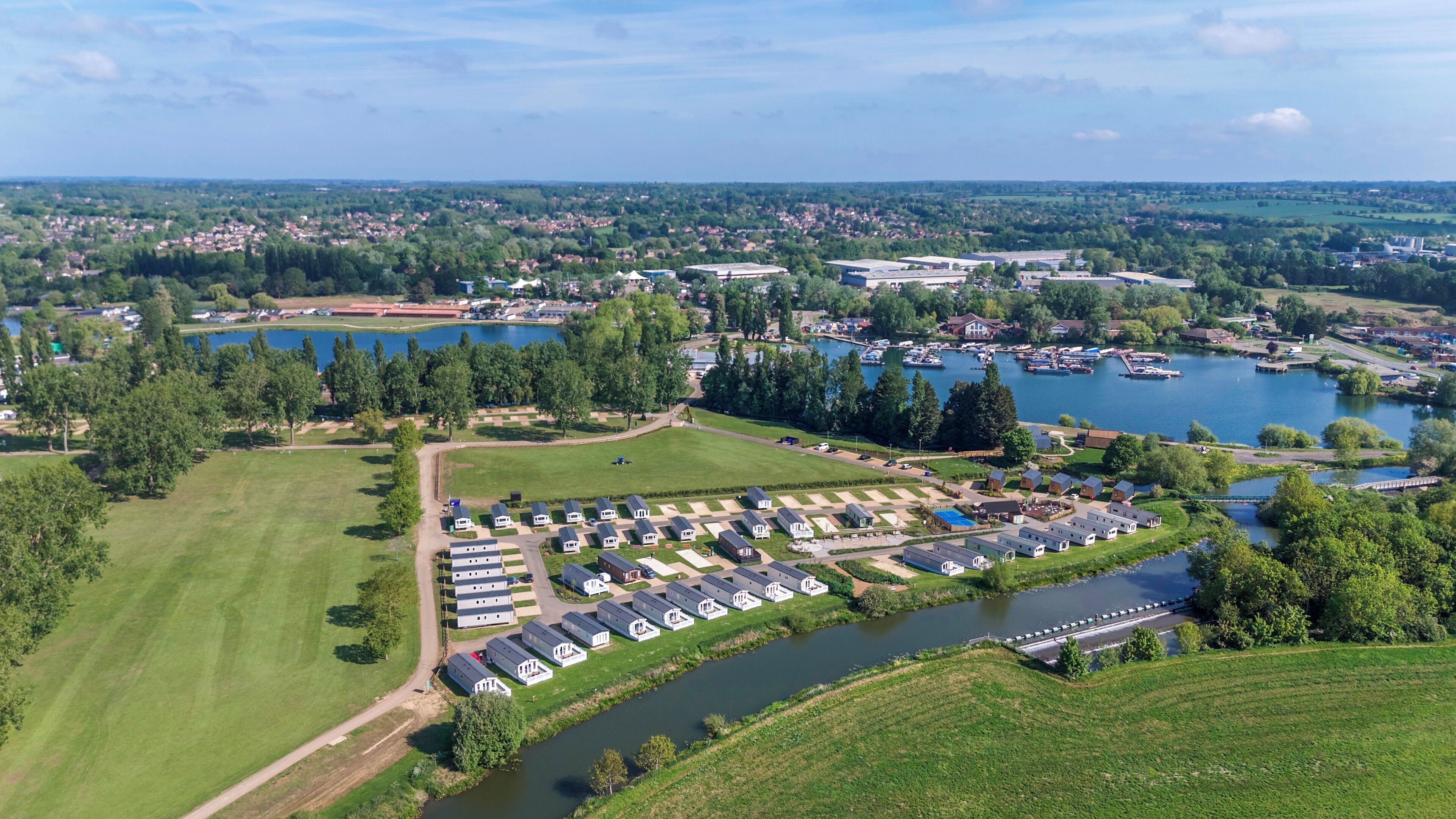 Vista aérea de un camping junto al lago con varias áreas para vehículos recreativos, un puerto deportivo y zonas residenciales circundantes.