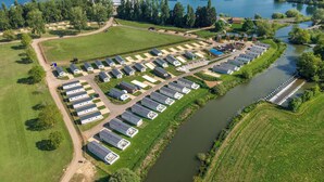 Luchtbeeld van een camping met campers en stacaravans, netjes op rijen langs een rivier.