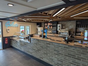 A gelato shop with a brick counter, a neon sign, a coffee machine, and a display of beverages. - Willowbrook Hideaway - Billing Aquadrome (Northampton)