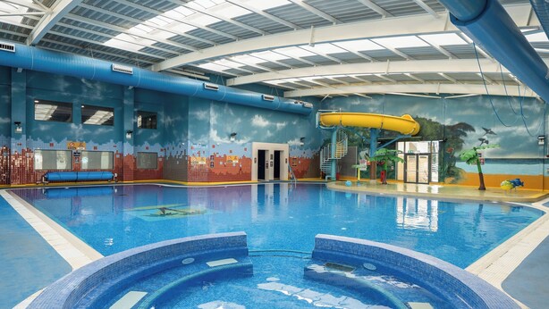 Une piscine intérieure avec un toboggan, un jacuzzi et une fresque représentant une scène de plage.