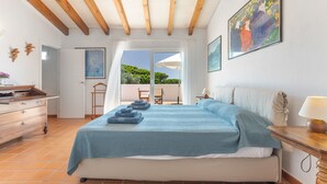 A bedroom with a bed, wooden ceiling beams, a window with a view, a desk, and a chair. - Villa 'Mottarone Cerca De Mar' with Private Pool, Wi-Fi and Air Conditioning (Sant Lluís)