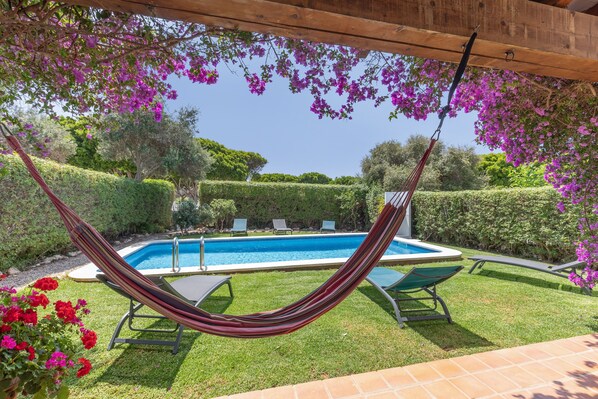 Zona de piscina con hamaca, sillas de descanso y vista despejada a la piscina.