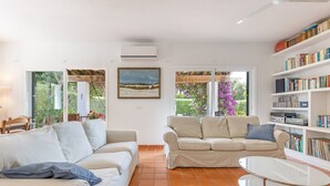A living room with two beige sofas, a white coffee table, and a bookshelf filled with books and DVDs. - Villa 'Mottarone Cerca De Mar' with Private Pool, Wi-Fi and Air Conditioning (Sant Lluís)