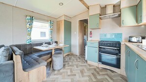 A compact kitchen with a stove, oven, and a dining area with a table and sofa. - Brookside Bliss - Billing Aquadrome (Northampton)