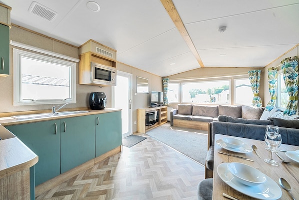 Interior compacto de una caravana con kitchenette, zona de estar y comedor.