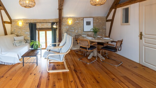 A cozy room with a wooden floor, a white sofa, a dining table with chairs, and a stone wall.