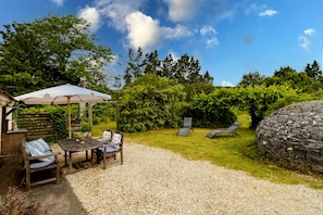 A patio area with a table and chairs, a covered seating area, and a view of a garden with trees and a rock.