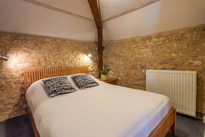 A bedroom with a stone wall, a wooden bed frame, a white mattress, and a radiator.