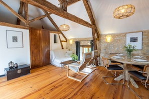 A loft-style room with exposed wooden beams, a dining area with a round table and chairs, a sofa, and a bed.