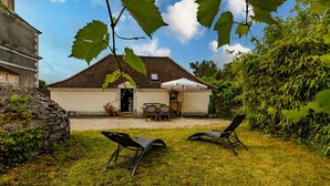A house with a patio, two lounge chairs, a table, and a white umbrella.