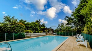 A rectangular swimming pool with a tiled deck, surrounded by a white fence, and a gazebo in the background.