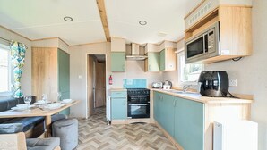 A compact kitchen with a microwave, toaster, and stove. There is a dining area with a table and chairs. - Brookside Bliss - Billing Aquadrome (Northampton)