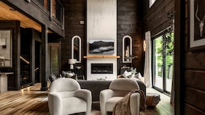 Un salon chaleureux avec une cheminée, deux fauteuils confortables et un grand téléviseur fixé au mur, juste au-dessus de la cheminée.