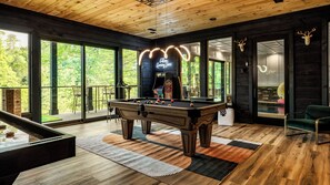 A pool table in a room with large windows, a neon sign, and wooden floors.
