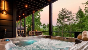 Un bain à remous avec vue sur les arbres, une terrasse en bois et un coucher de soleil.