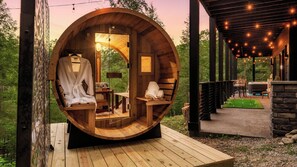 A wooden barrel-shaped room with a bench, a table, and a hanging robe.