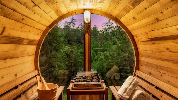 Un sauna en bois doté d’une ouverture circulaire, d’un banc en bois, d’une table de sauna et d’une serviette.