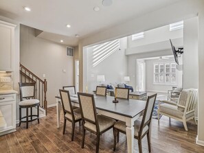Ein geräumiger Essbereich mit Holztisch und Stühlen, eine Treppe, die zu einer anderen Ebene führt, und Blick auf ein Wohnzimmer mit Sofa und Lampen.