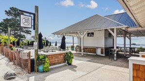 A coastal restaurant with outdoor seating, a sign indicating the address, and a view of the sea.